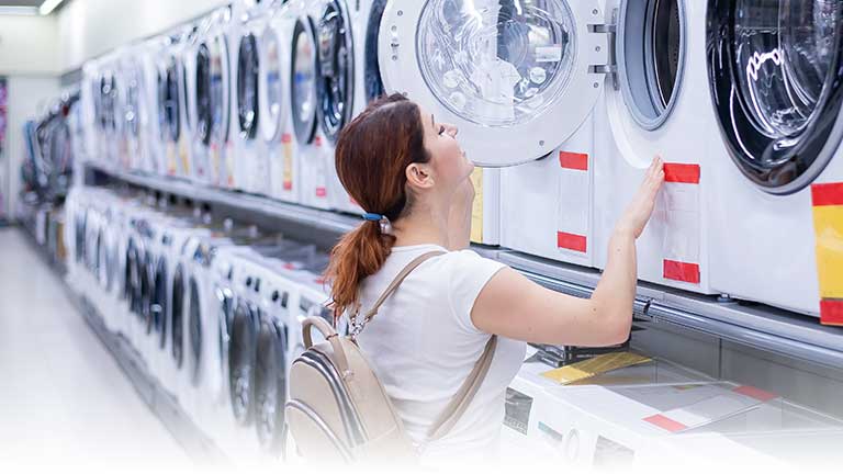 A young woman shopping for washing machines in a big box store.