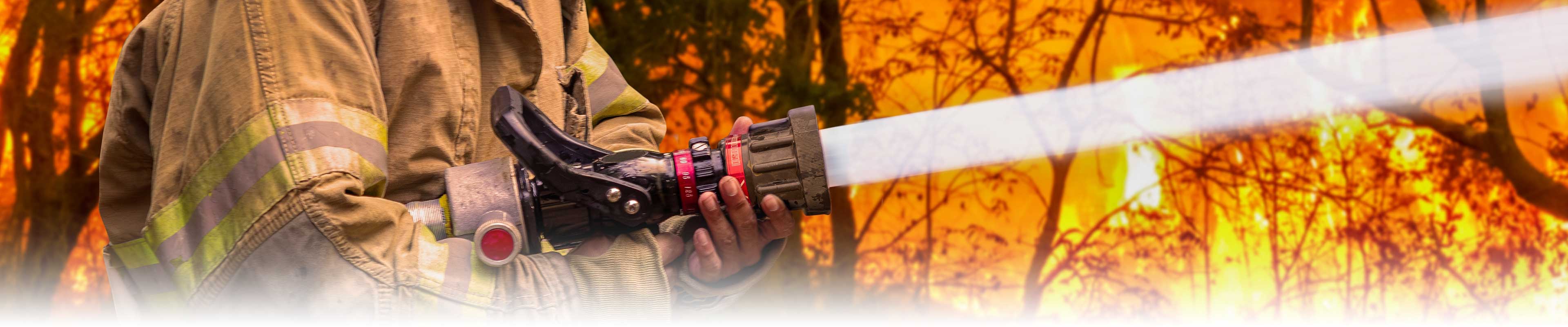 A wildfire firefighter spraying flames with water from a large hose.