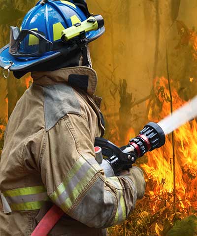 A wildfire firefighter spraying flames with water from a large hose.