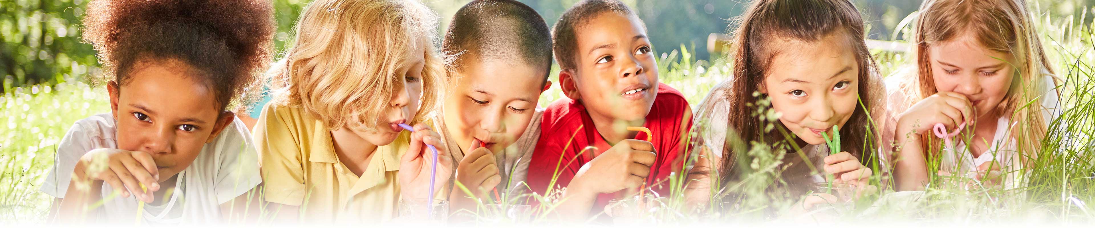 Five children lying in tall grass sipping-drinks from straws.