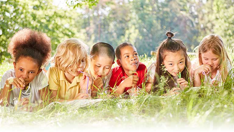 Five children lying in tall grass sipping-drinks from straws.