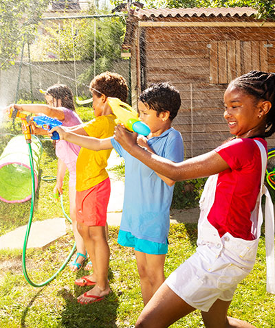Four children playing with water guns and hoses.