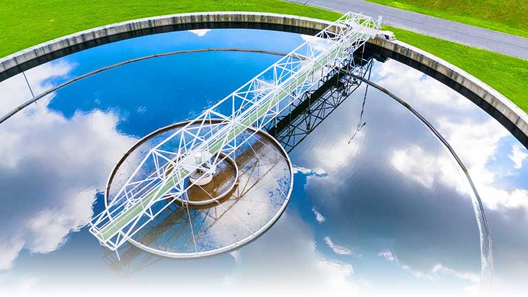 A wastewater treatment plant tank reflecting a cloudy sky.
