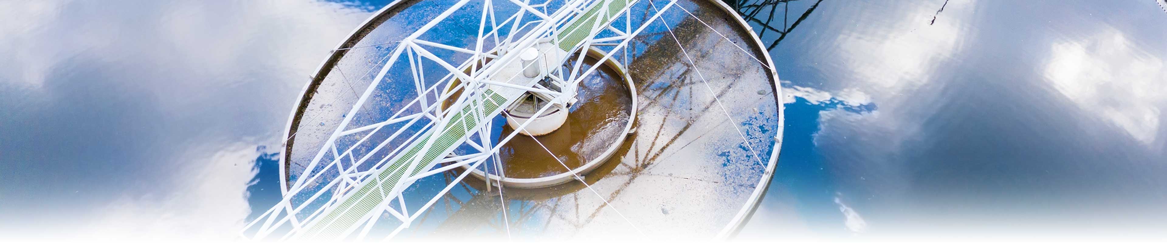 A wastewater treatment plant tank reflecting a cloudy sky.
