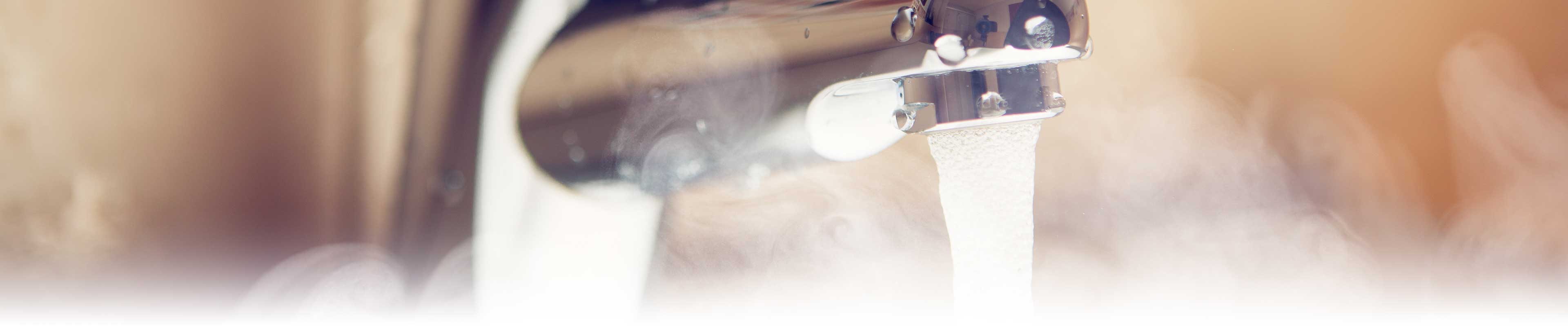 An open bathroom tap with hot water and steam coming out.