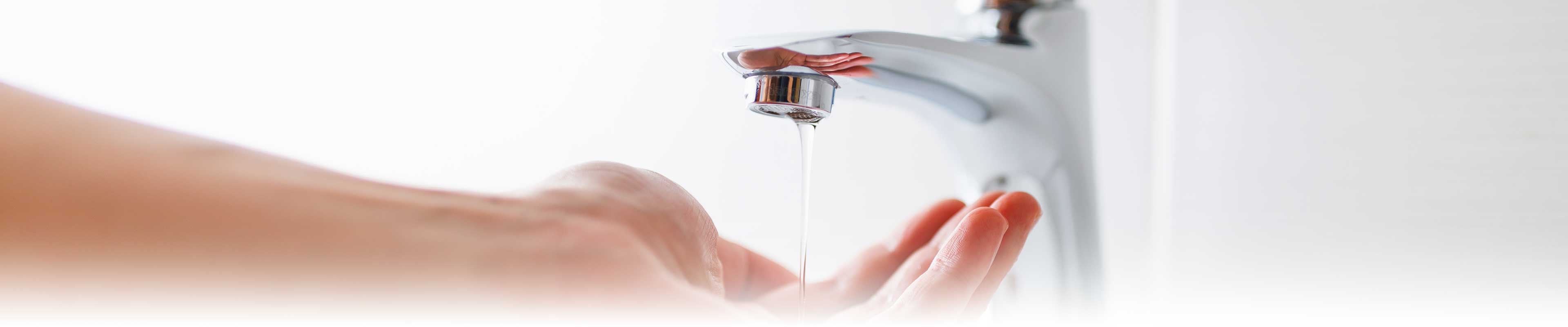 A hand under an open bathroom tap with only a trickle of water.
