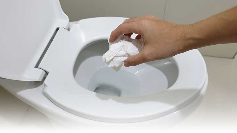 A hand disposing of non-flushable wipes in a toilet.