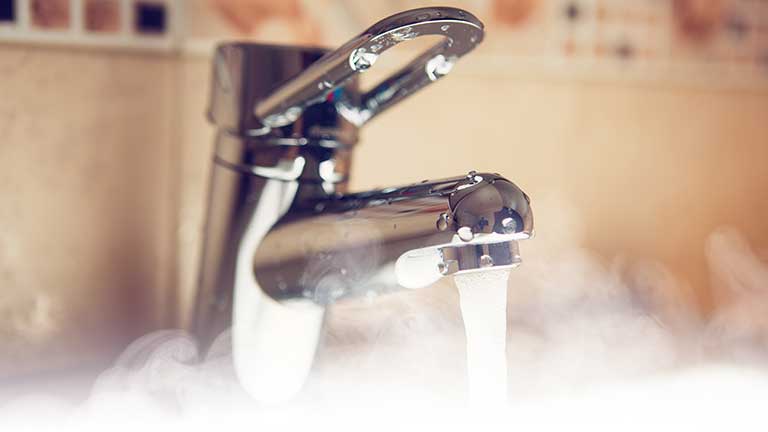 An open bathroom tap with hot water and steam coming out.