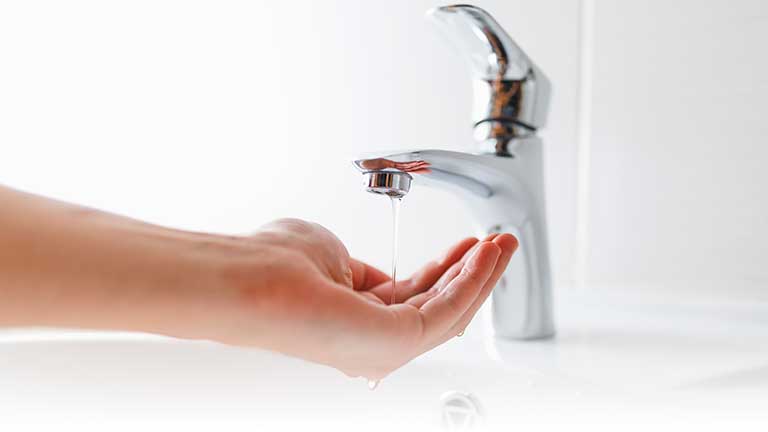 A hand under an open bathroom tap with only a trickle of water.