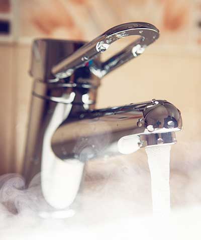 An open bathroom tap with hot water and steam coming out.