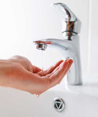 A hand under an open bathroom tap with only a trickle of water.