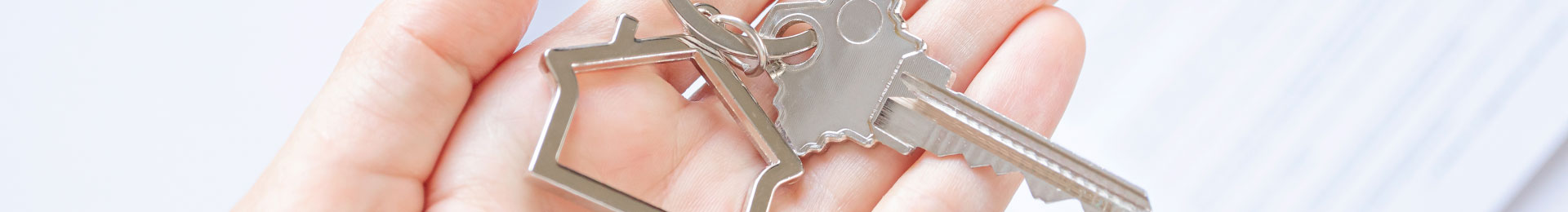Close-up of a woman's hand holding a house-shaped key chain and single key.