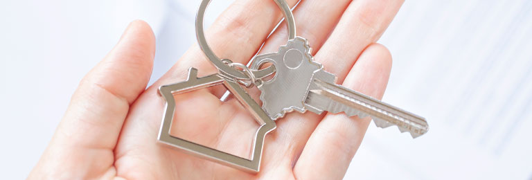 Close-up of a woman's hand holding a house-shaped key chain and single key.