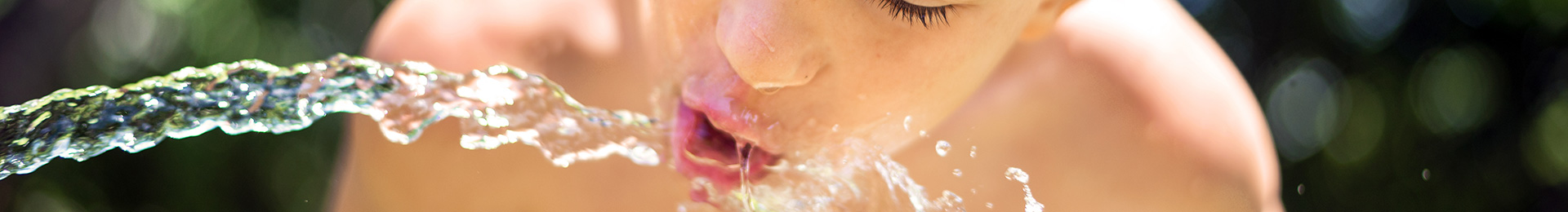 Boy drinking water from a water hose.