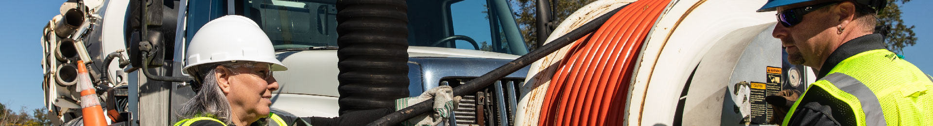 Two workers operating a sewer vacuum truck.