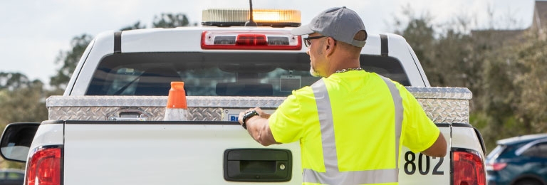 A worker standing behind a utility service pickup truck.