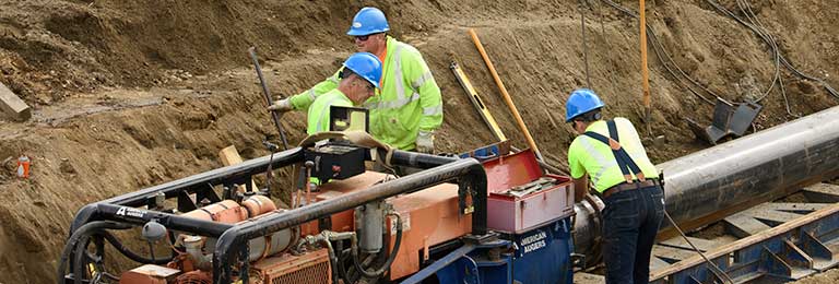 Workmen laying a watermain in a deep excavation.