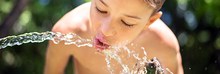 Boy drinking water from a water hose.