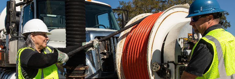 Two workers operating a sewer vacuum truck.