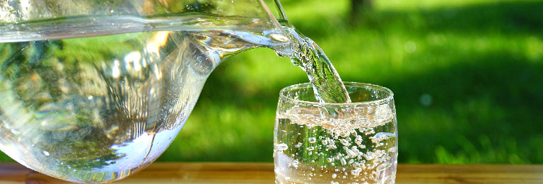 Crystal clear water being poured from a pitcher into a glass.